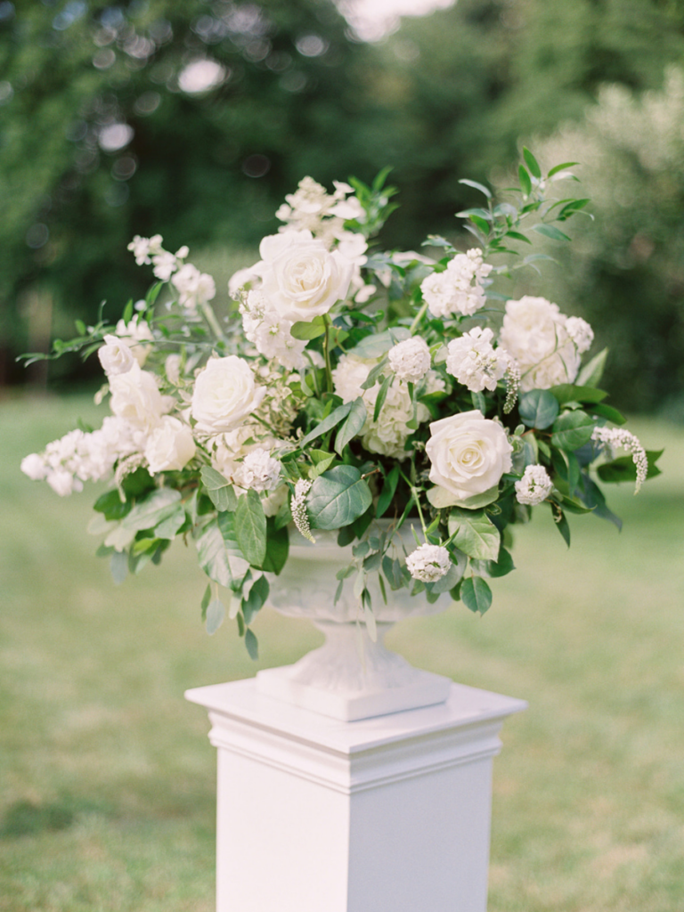 Detailed photo of large white urn floral arrangement. Filled with white roses, stock, lisianthus, scabiosa and lots of greenery