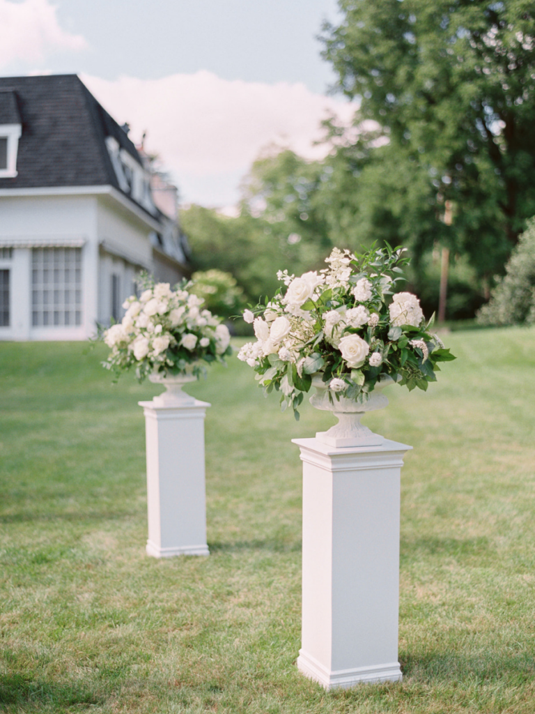 Two large urns filled with lush white floras on pedestals at the ceremony spot at Landgon Hall