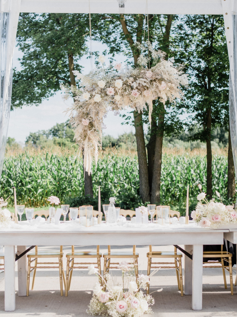 Decorated head table with blush and white accents and a floral cloud installation filled with blush and white roses, baby's breath and dried florals 
