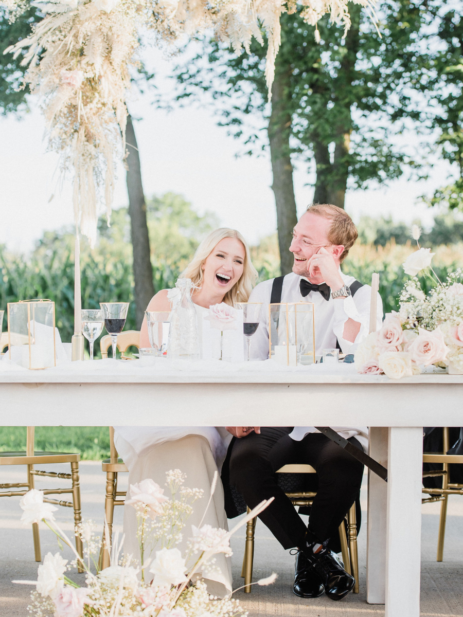 The newly wed couple laughing at their head table with a floral cloud installation above them