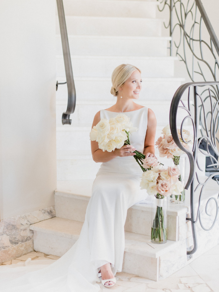 Bride sitting on the staircase hold her modern bouquet filled with white long stemmed roses