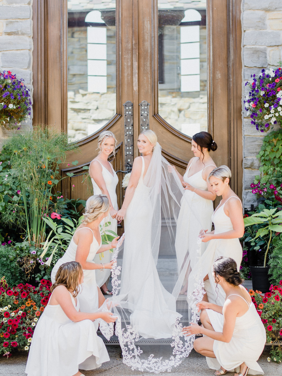 Bride standing with her bridesmaids around her fixing her veil and posing 