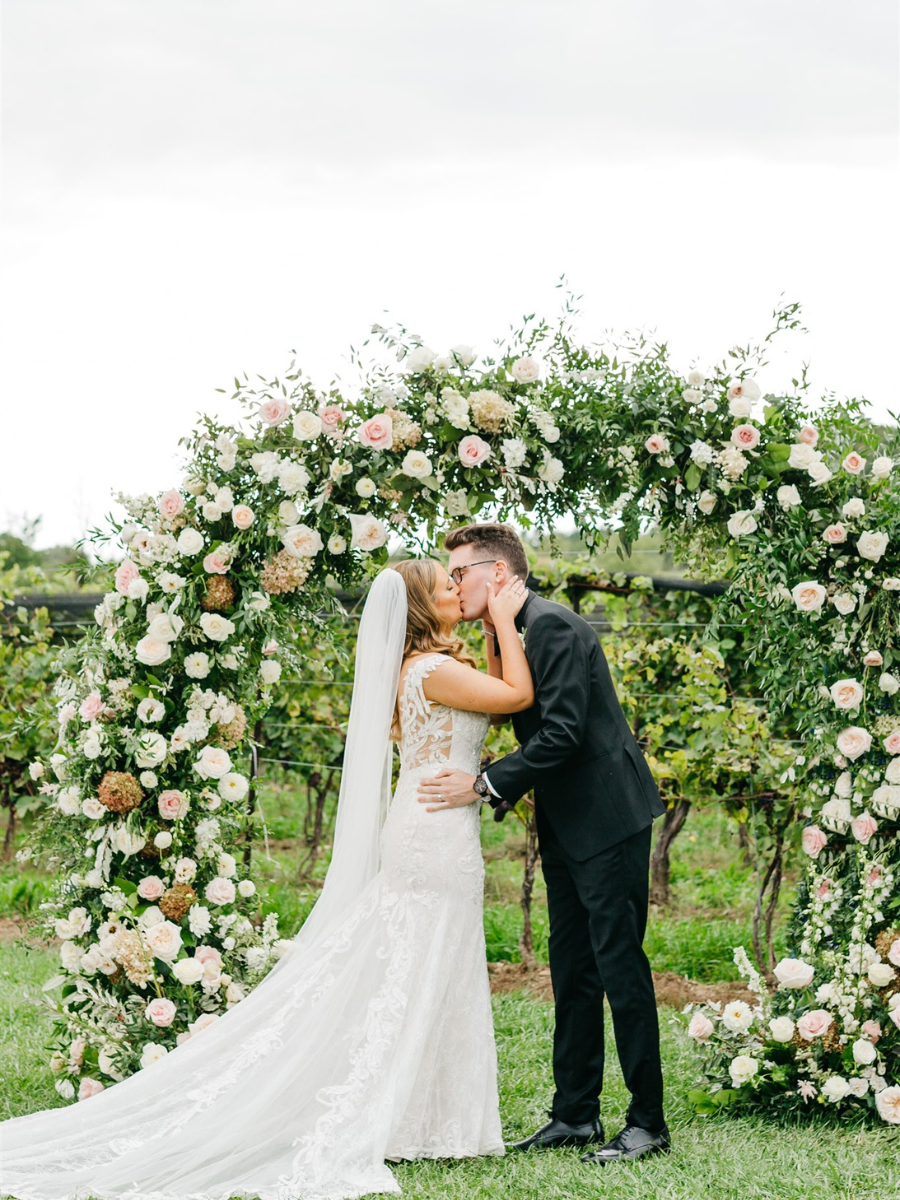 Bride & Groom sharing their first kiss at the alter in front of lush floral arbour