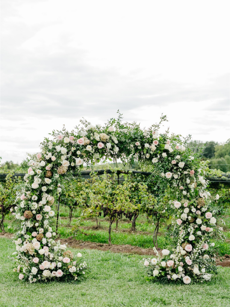 Finished floral circle arbour located at the alter filled with lots of blush, white and cream florals with mixed greenery winery vineyard 