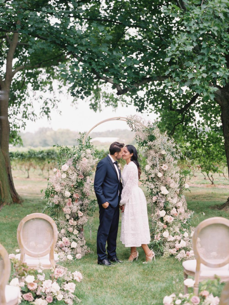 Bride & groom kissing in front of floral arch at their ceremony