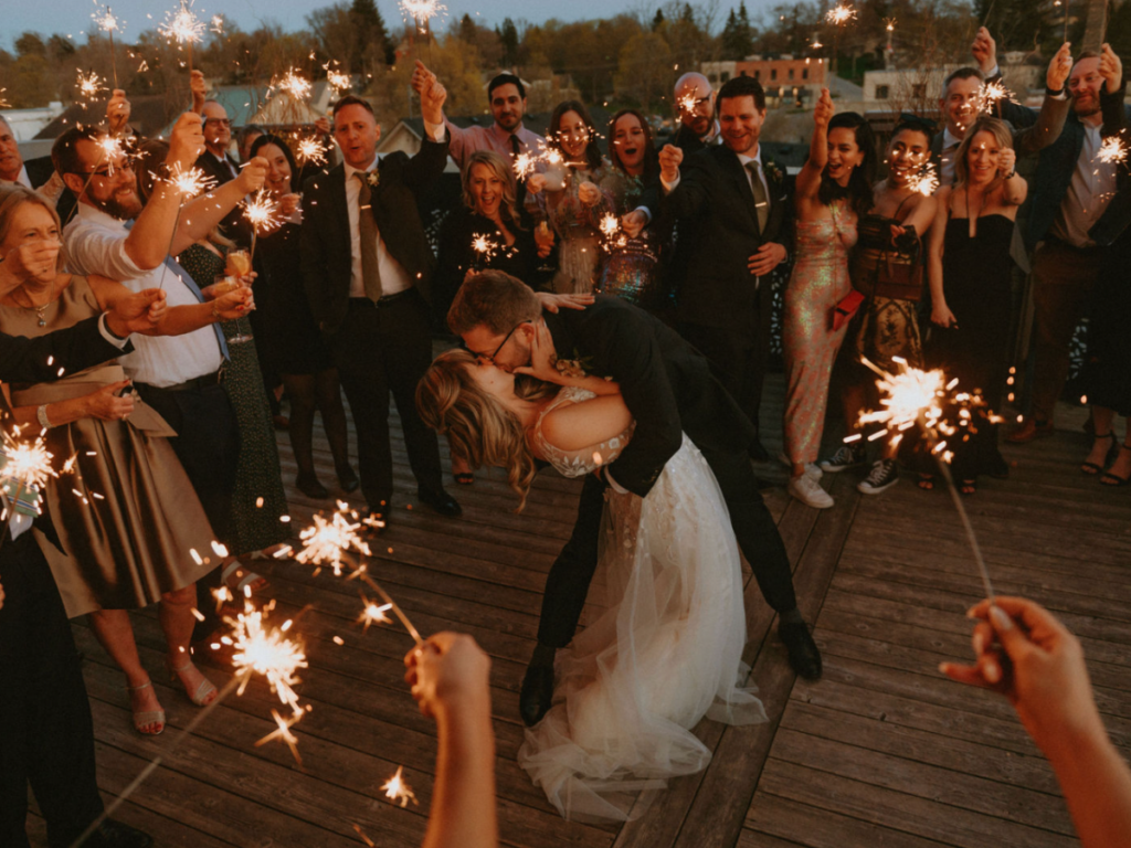 Bride and groom at the end on the night on the roof top patio at the Elora Mill surrounded by their guests holding sparklers 