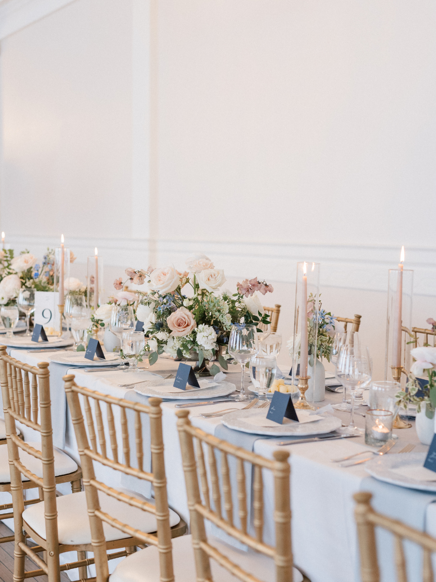 Long table filled with lit candles,, lots of flowers and blue table accents 