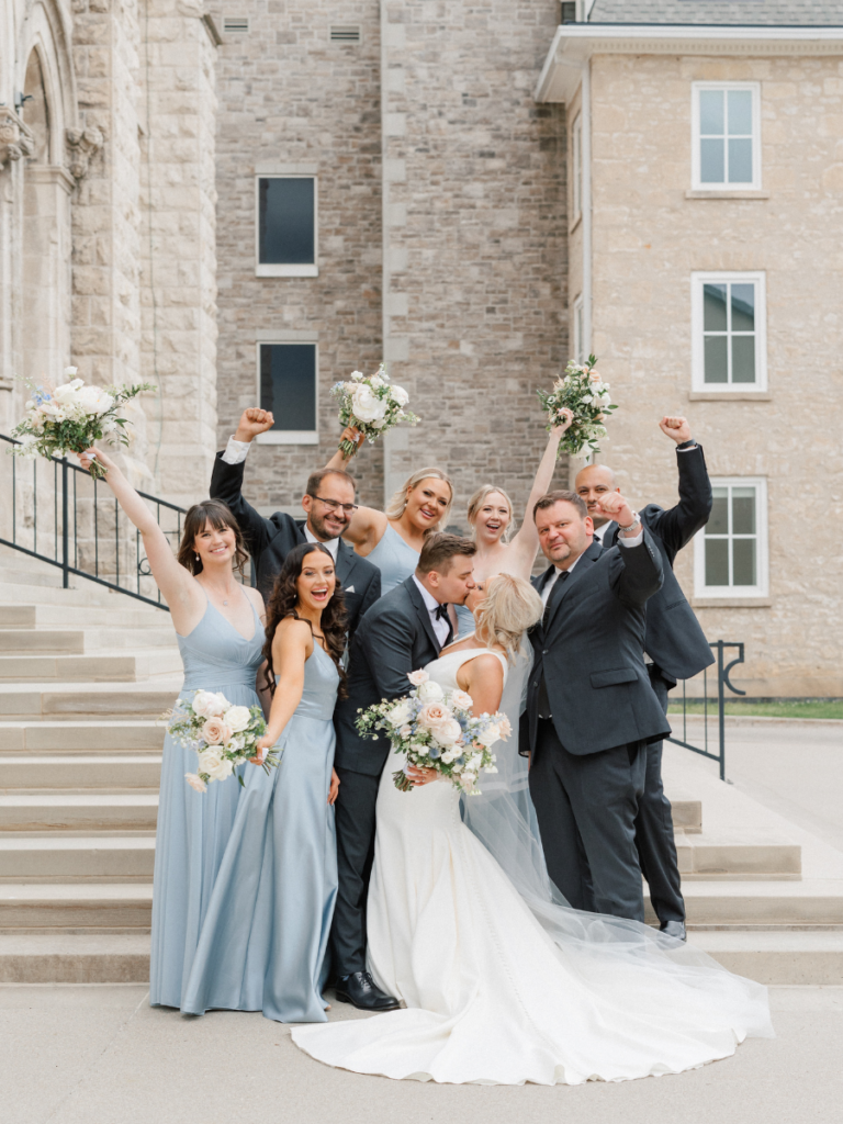 Bride and groom kissing while their bridal party celebrates around them