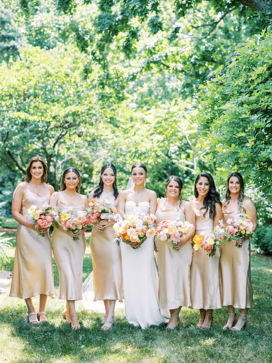 Bride and her bridesmaids holding their colourful bouquets. Bridesmaids wearing champagne satin dresses.