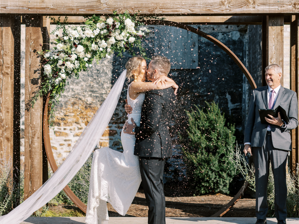 Bride and groom sharing their first kiss as newlyweds at their Elora Mill wedding with confetti in the air